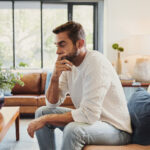 Stressed man sitting on couch with head in hand, reflecting the impact of chronic stress on cardiovascular and arterial health