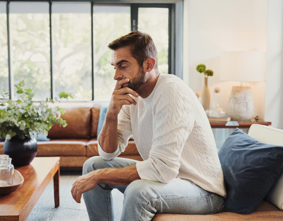 Stressed man sitting on couch with head in hand, reflecting the impact of chronic stress on cardiovascular and arterial health