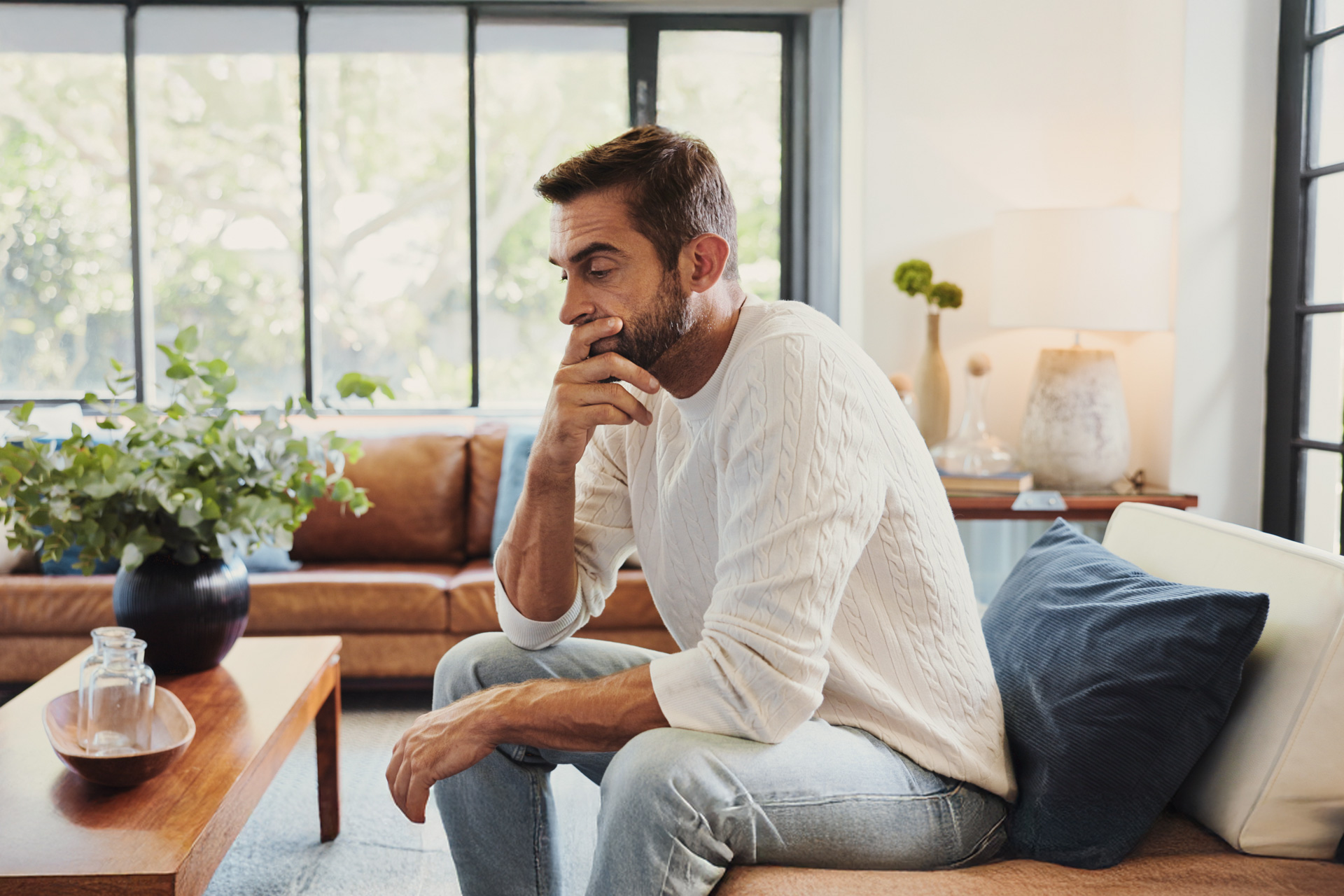 Stressed man sitting on couch with head in hand, reflecting the impact of chronic stress on cardiovascular and arterial health